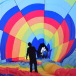 Silhouette of a man stands and looks up inside a colorful hot air balloon