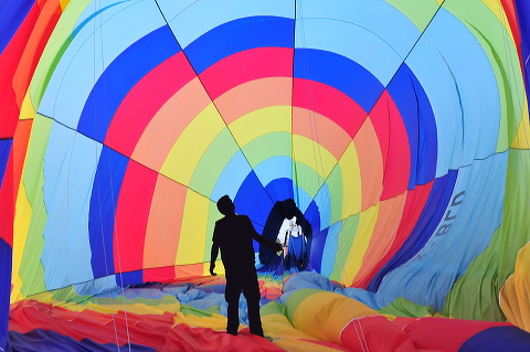 Silhouette of a man stands and looks up inside a colorful hot air balloon