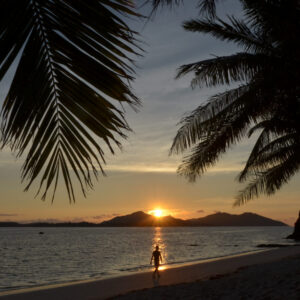 Silhouette of one unrecognizable person walking on empty exotic tropical beach during dramatic sunset in the Yasawa Islands, Fiji.