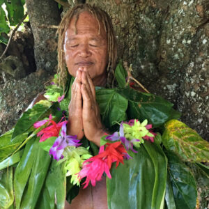 Old aged Pacific Islander man praying under a rain forest tree