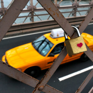 Padlock with red heart on Brooklyn Bridge while Yellow medallion Taxi cab drives on the under pass to Manhattan New York, USA.