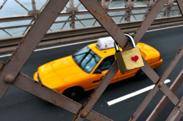 Padlock with red heart on Brooklyn Bridge while Yellow medallion Taxi cab drives on the under pass to Manhattan New York, USA.