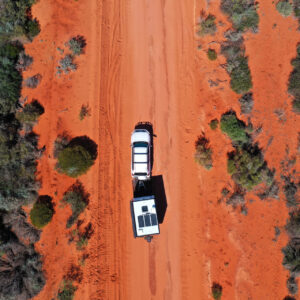 Aerial landscape drone view of 4WD vehicle towing an off road caravan driving on a sand dirt road at Peron Peninsula in Shark Bay, Western Australia.