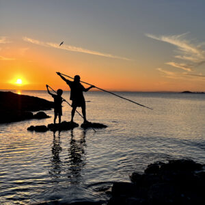 Silhouette image of first nation Australian aboriginal people, father and son, using spears to hunt seafood in Cape York Queensland, Australia.