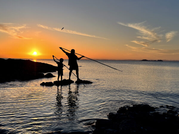 Silhouette image of first nation Australian aboriginal people, father and son, using spears to hunt seafood in Cape York Queensland, Australia.