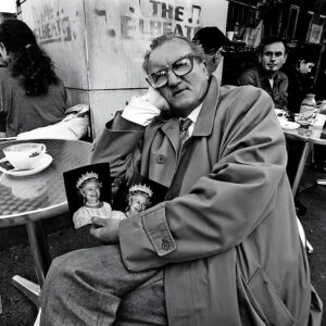 Queen of Hearts Active senior British man sitting in cafe in Soho London holding photos of Queen Elizabeth II – Fine art photography print for sale. Decoration poster for home or office wall taken by documentary travel photographer Rafael Ben Ari