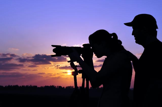 Silhouette of professional documentary travel photographer teaching a young adult woman student photography outdoors during sunset.Real people. Copy space