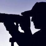 Silhouette of a photographer wearing a hat, camera and tripod with a blue sky background