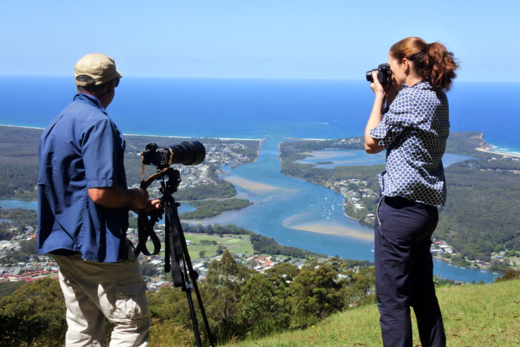 Documentary travel photographer is teaching a female student how to take an aerial landscape view photo of Camden Heaven River with a telephoto lens on a tripod in New South Wales, Australia