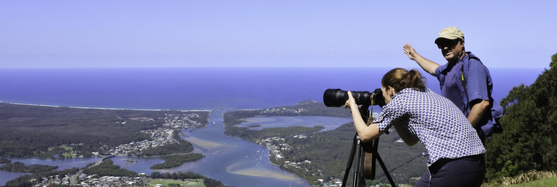 Documentary travel photographer is teaching a female student how to take an aerial landscape view photo of Camden Heaven River with a telephoto lens on a tripod in New South Wales, Australia