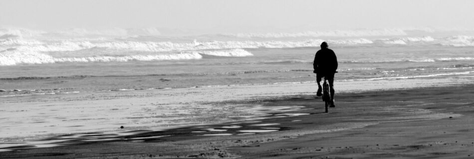 A man rides a bike over Ninety Mile Beach in Northland New Zealand.